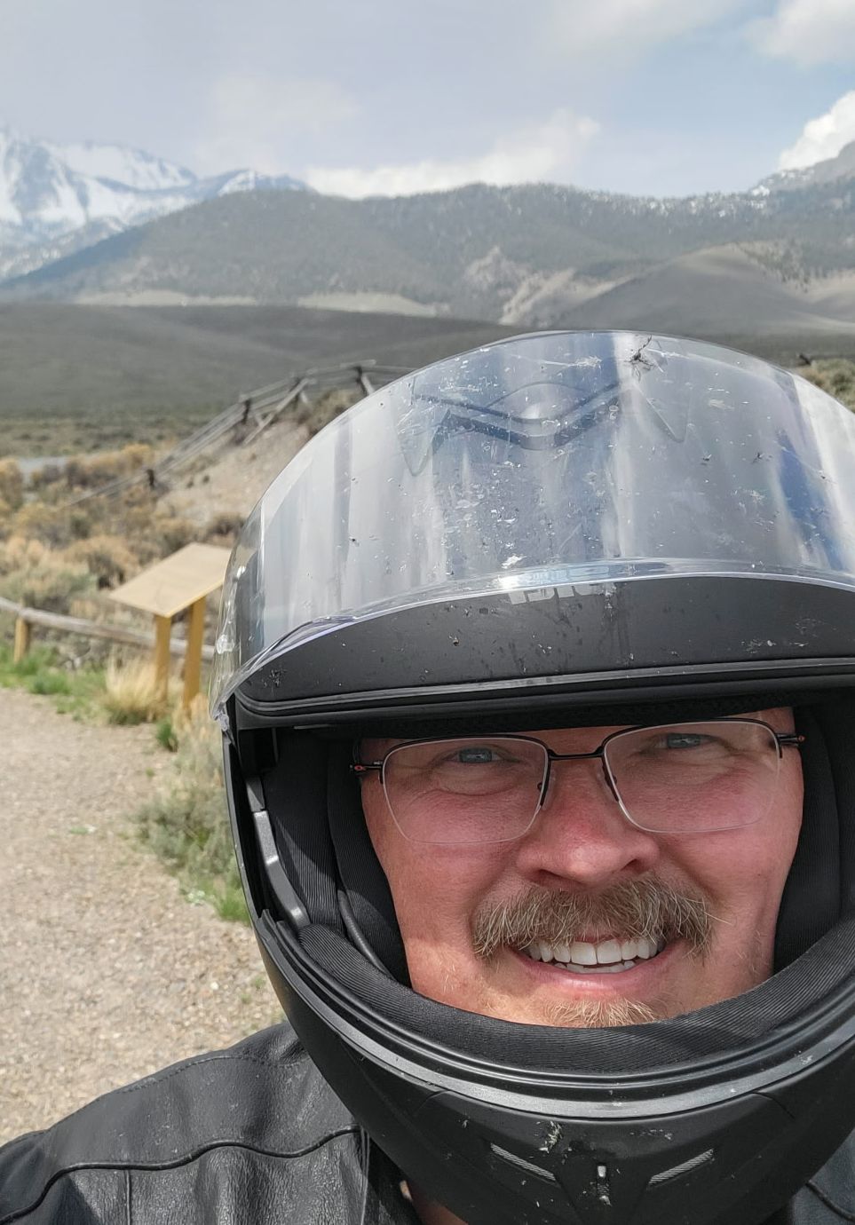 Joe States smiling in his helmet on the trail, snow-capped peaks rising behind him