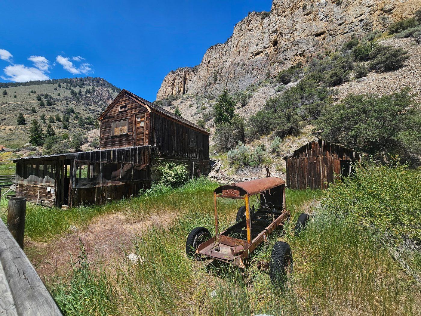 Ghost town ruins with a rusted antique truck beneath limestone cliffs in central Idaho
