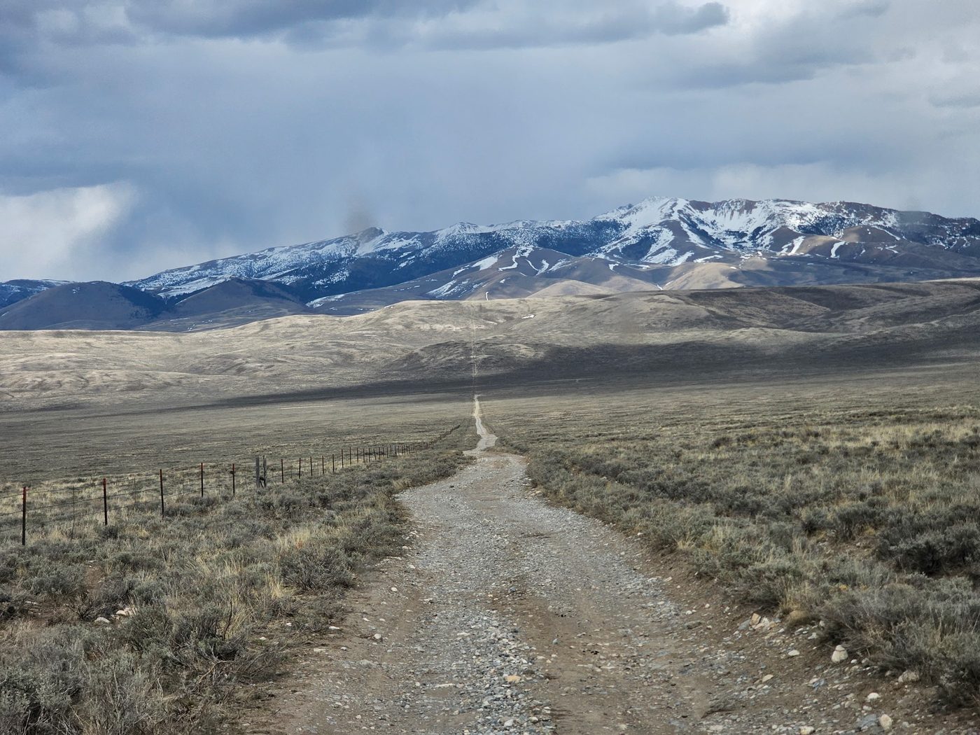 A long gravel road running straight toward distant snow-capped mountains